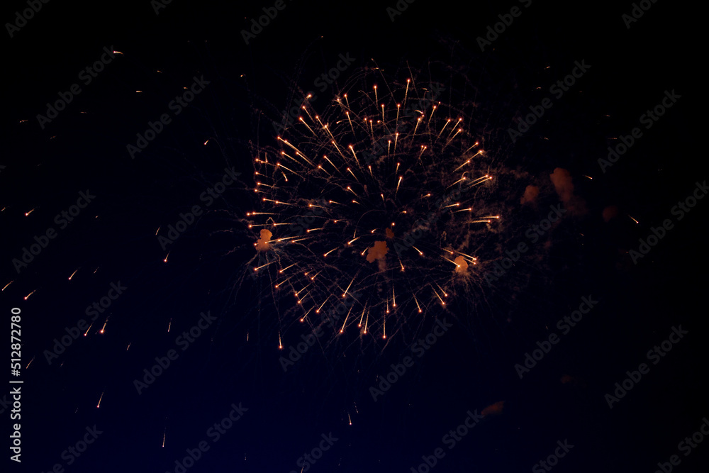 A bright ball of fireworks with orange sparks and a lot of sparks around on the background of the night sky. High quality photo