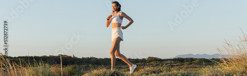 fit woman in shorts and sports bra listening music and running outside, banner.