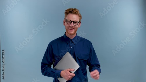 portrait of smiling young IT specialist with laptop in blue studio