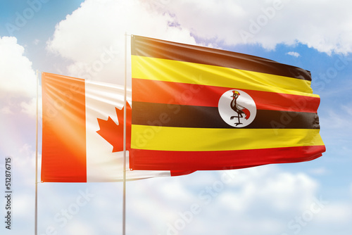 Sunny blue sky and flags of uganda and canada