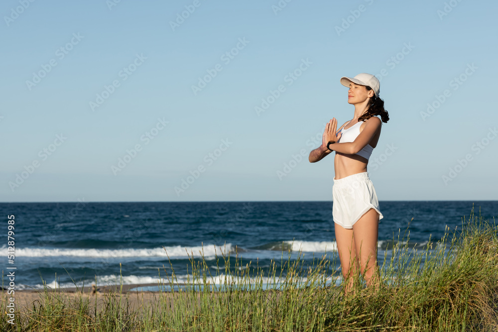 young fit woman in shorts and sports bra meditating near blue sea on beach. young fit woman in shorts and sports bra meditating near blue sea on beach.