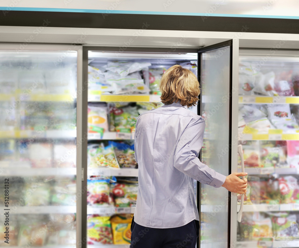 Man choosing frozen food from a supermarket freezer... choosing a dairy products at supermarket, reading product information Man choosing frozen food from a supermarket freezer... choosing a dairy products at supermarket, reading product information