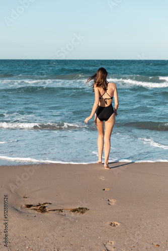 back view of brunette woman in black swimwear walking into sea.