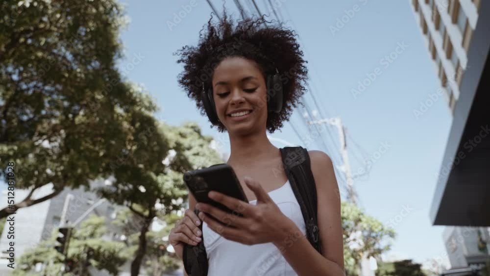 Beautiful young Latin woman using smartphone standing on city street. Portrait of Latina smiling female using mobile phone. Cinematic 4K