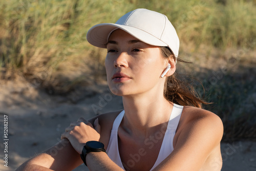 Burnette sportswoman in baseball cap listening music in wireless earphone on beach. photo