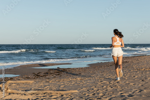 back view of young sportive woman jogging near sea in summer.