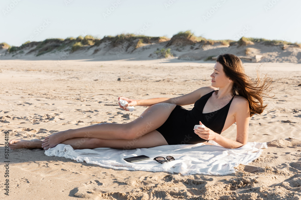 young woman lying on blanket and applying spf sunscreen on body.