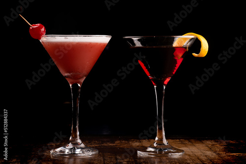 Two martini glasses with cherry cocktails and red liquid and orange shavings