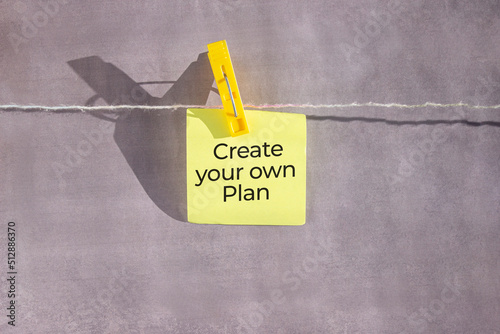 Create your own Plan text on a yellow sticker on a rope with clothespins on a grey background.