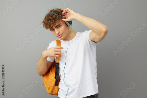 a student guy stands on a gray background in a white T-shirt and listening to music with headphones clutched his head looking at the camera with his eyes wide open