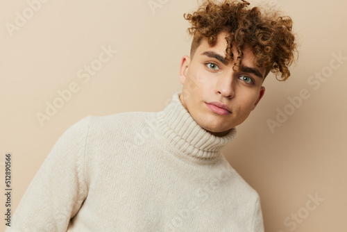 a close horizontal portrait of a handsome, handsome man standing on a beige background in a light turtleneck, looking pleasantly into the camera