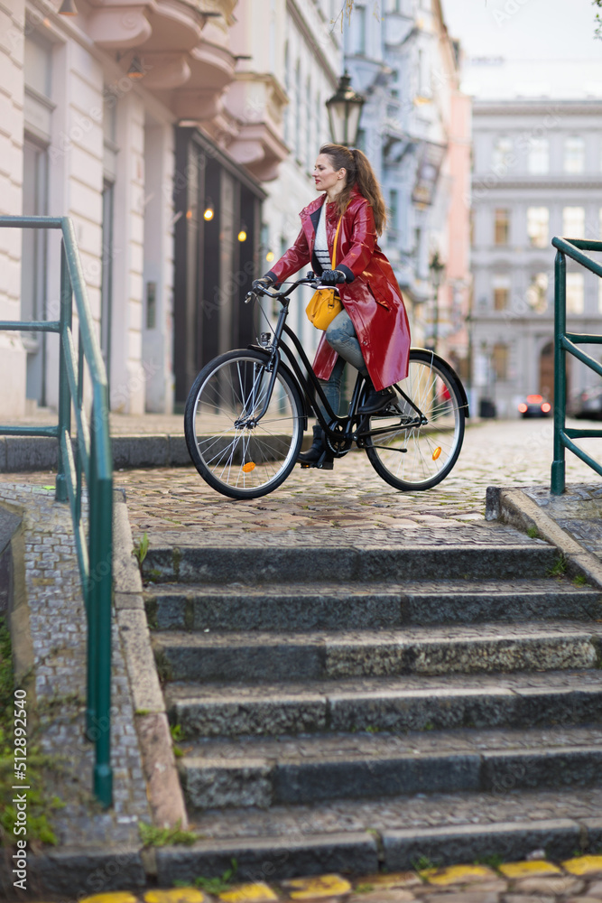modern woman in red rain coat outdoors in city riding bicycle