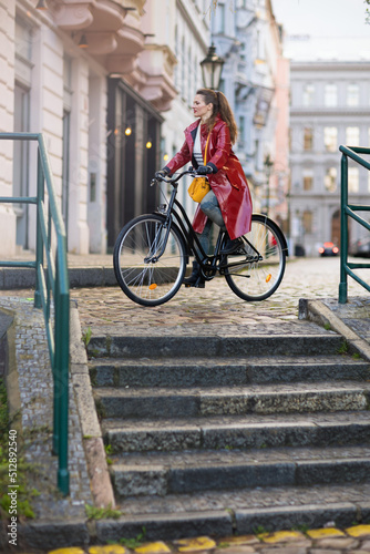 Fototapeta Naklejka Na Ścianę i Meble -  modern woman in red rain coat outdoors in city riding bicycle