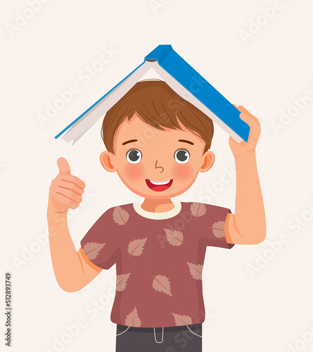 cute little boy student holding book on his head showing thumb up