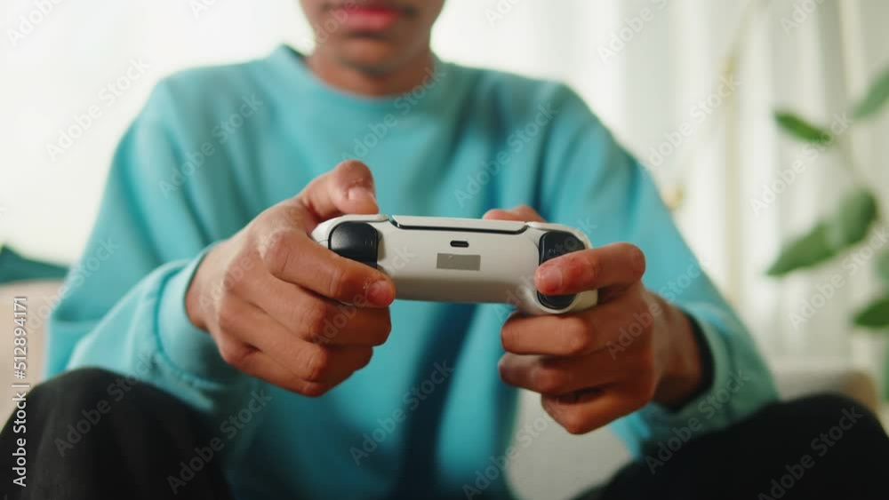 African American man playing video games on modern console. Happy young guy sitting on sofa in living room, cheerful teenager using white gamepad, enjoying AR 3D game. African American man playing video games on modern console. Happy young guy sitting on sofa in living room, cheerful teenager using white gamepad, enjoying AR 3D game.