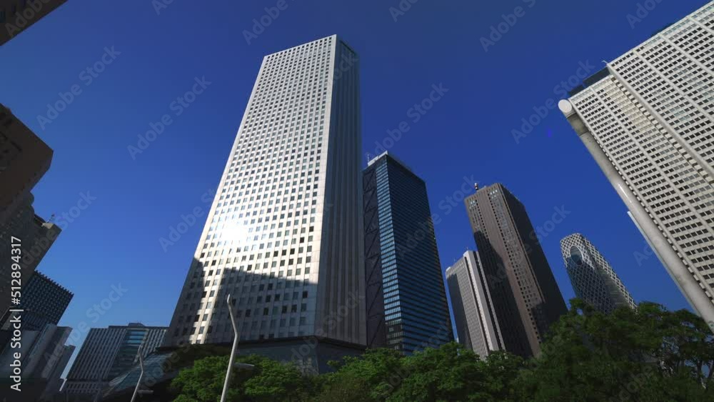 Nishi-Shinjuku skyscraper stands beyond fresh green trees growing on the roadway in Shinjuku subcenter district at Shinjuku, Tokyo, Japan on May 04, 2022. Nishi-Shinjuku skyscraper stands beyond fresh green trees growing on the roadway in Shinjuku subcenter district at Shinjuku, Tokyo, Japan on May 04, 2022.