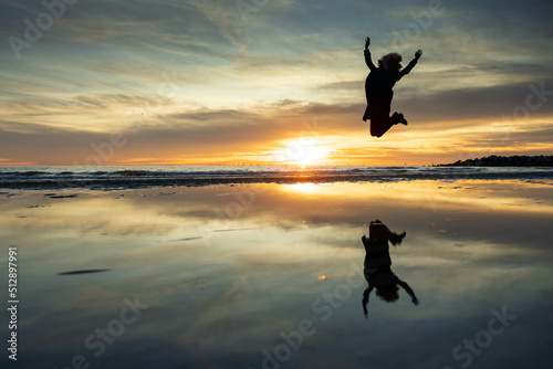 Jumping Curly Hair Woman Silhouette in Mid Air Against Sunset on a Empty Beach