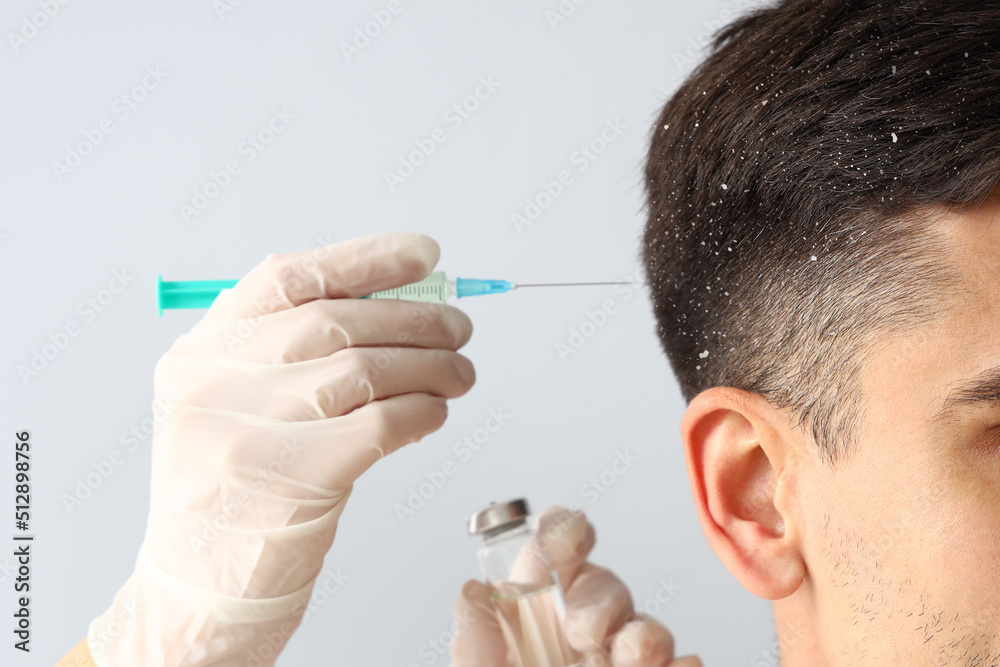 Young man with problem of dandruff receiving injection on light background, closeup