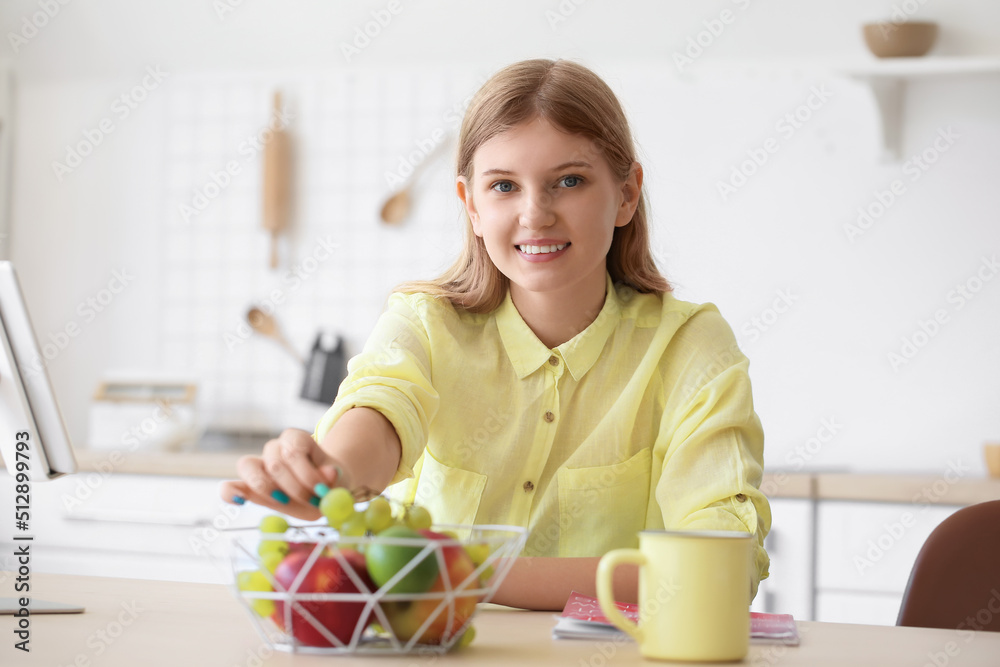 Teenage girl taking grape from basket at table in kitchen Teenage girl taking grape from basket at table in kitchen
