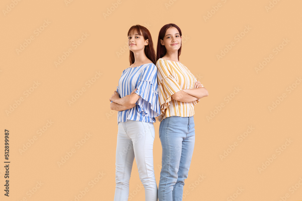 Teenage twin sisters on beige background - obrazy, fototapety, plakaty 