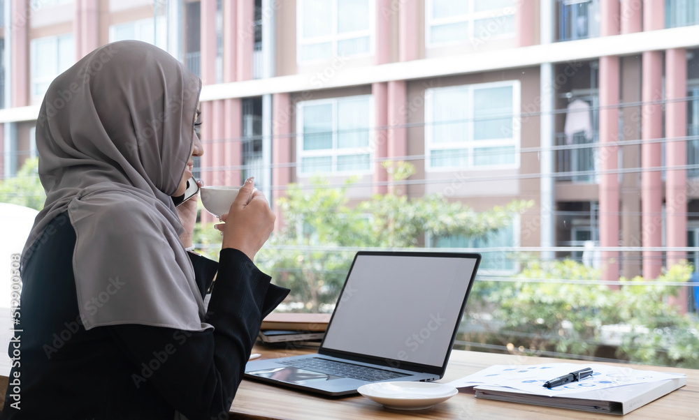 happy beautiful muslim female worker holding hot coffee mug sitting in office and using mobile cell phone viewing online news relaxing. happy beautiful muslim female worker holding hot coffee mug sitting in office and using mobile cell phone viewing online news relaxing.
