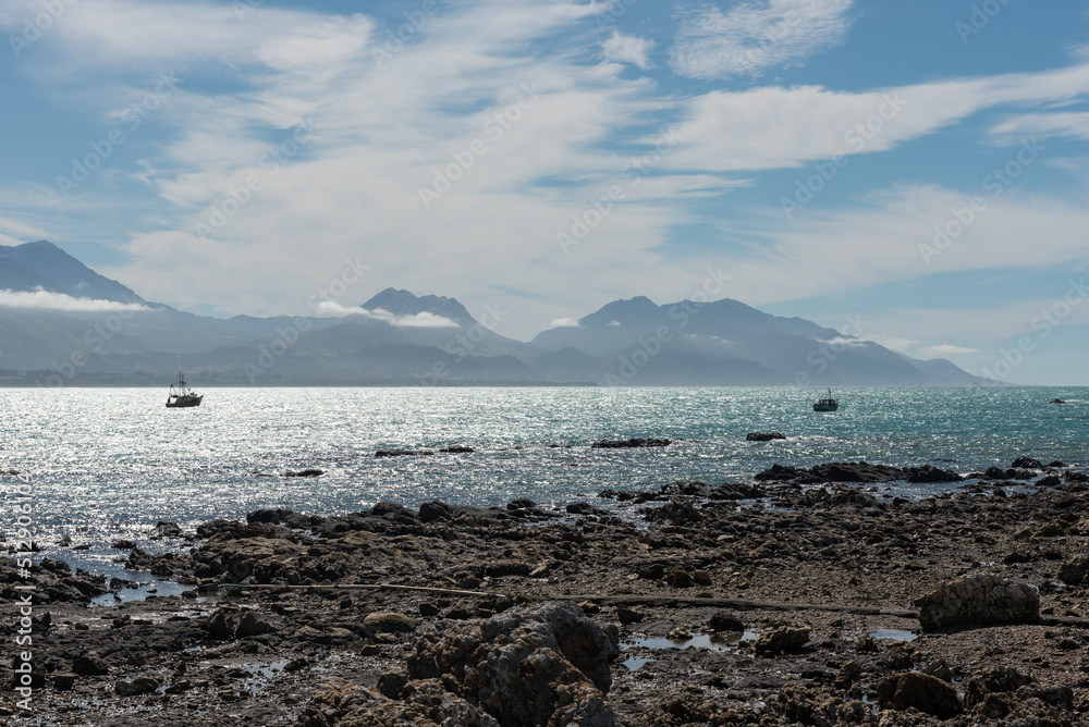 The view across the bay at Kaikoura from the peninsula to the Kaikoura Ranges. Two commercial fishing boats at anchor offshore. Kaikoura, Canterbury, South Island, New Zealand. The view across the bay at Kaikoura from the peninsula to the Kaikoura Ranges. Two commercial fishing boats at anchor offshore. Kaikoura, Canterbury, South Island, New Zealand.