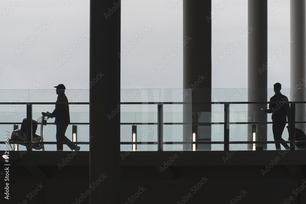 Fototapeta premium Silhouette of people with luggage walking in an airport, with copy space.