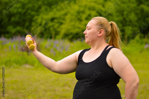 Portrait of cheerful aged woman in fitness wear exercising with yellow dumbbells in park.