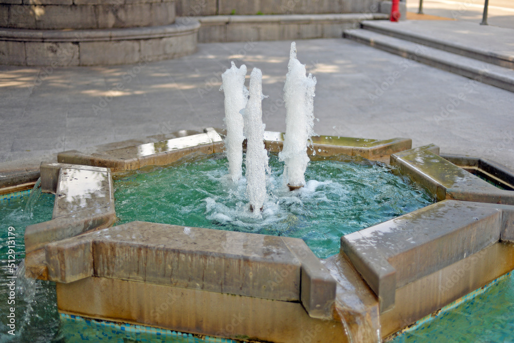 A small fountain with clear water. Concrete , masonry. Empty square.