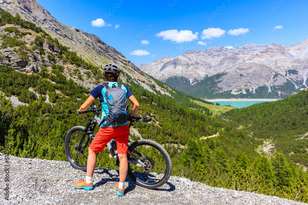 Woman tourist with mtb bike looking at beautiful Alpisella valley on sunny summer day, Alps Mountains, Italy