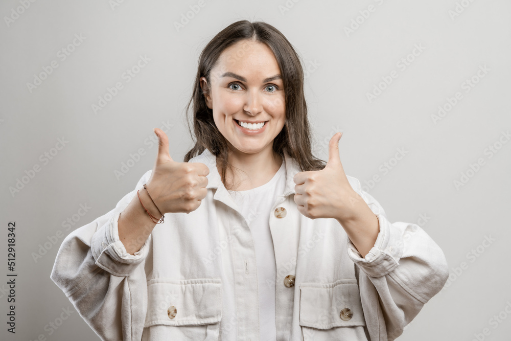 Brunette girl with long hair on a gray background. The girl gives a thumbs up Brunette girl with long hair on a gray background. The girl gives a thumbs up
