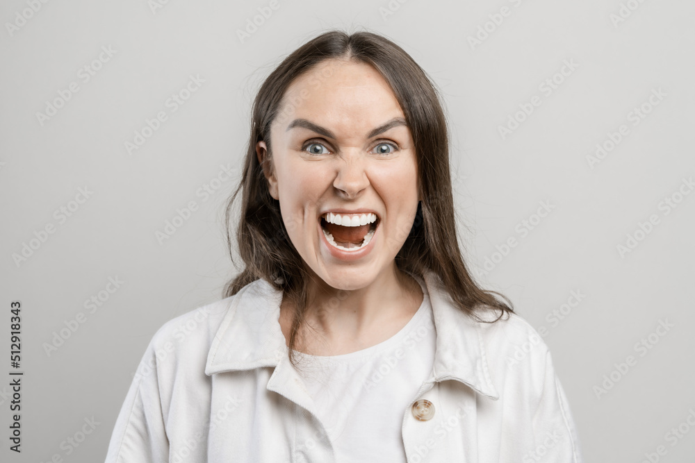 Brunette girl with long hair on a gray background. The girl screams with anger Brunette girl with long hair on a gray background. The girl screams with anger