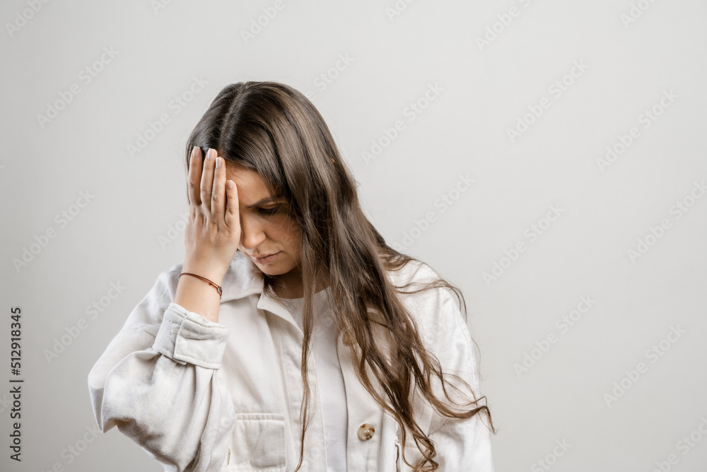 Migraine and headaches in women. Brunette girl with long hair on a gray background Migraine and headaches in women. Brunette girl with long hair on a gray background