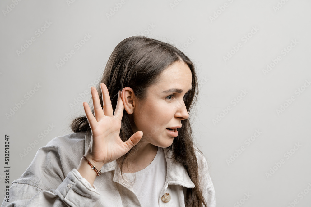 Woman is eavesdropping on a conversation. Brunette girl with long hair on a gray background Woman is eavesdropping on a conversation. Brunette girl with long hair on a gray background