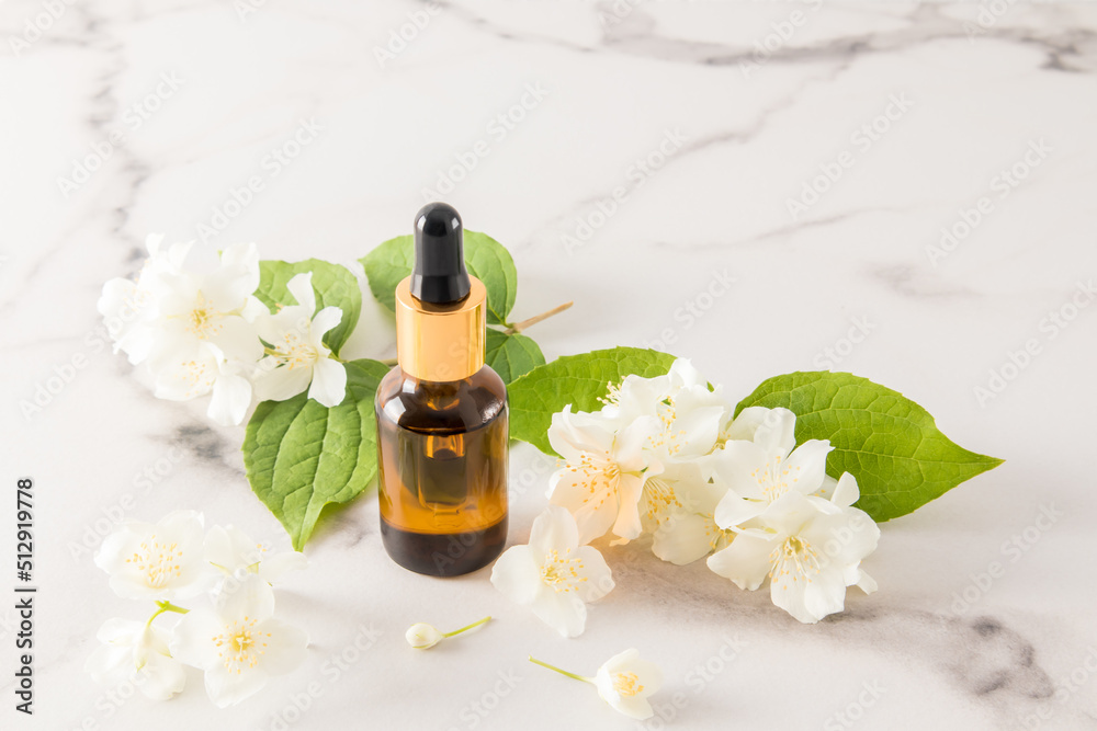 whey based on jasmine oil in a cosmetic bottle of brown glass on a marble white background and fresh flowers of garden jasmine. whey based on jasmine oil in a cosmetic bottle of brown glass on a marble white background and fresh flowers of garden jasmine.
