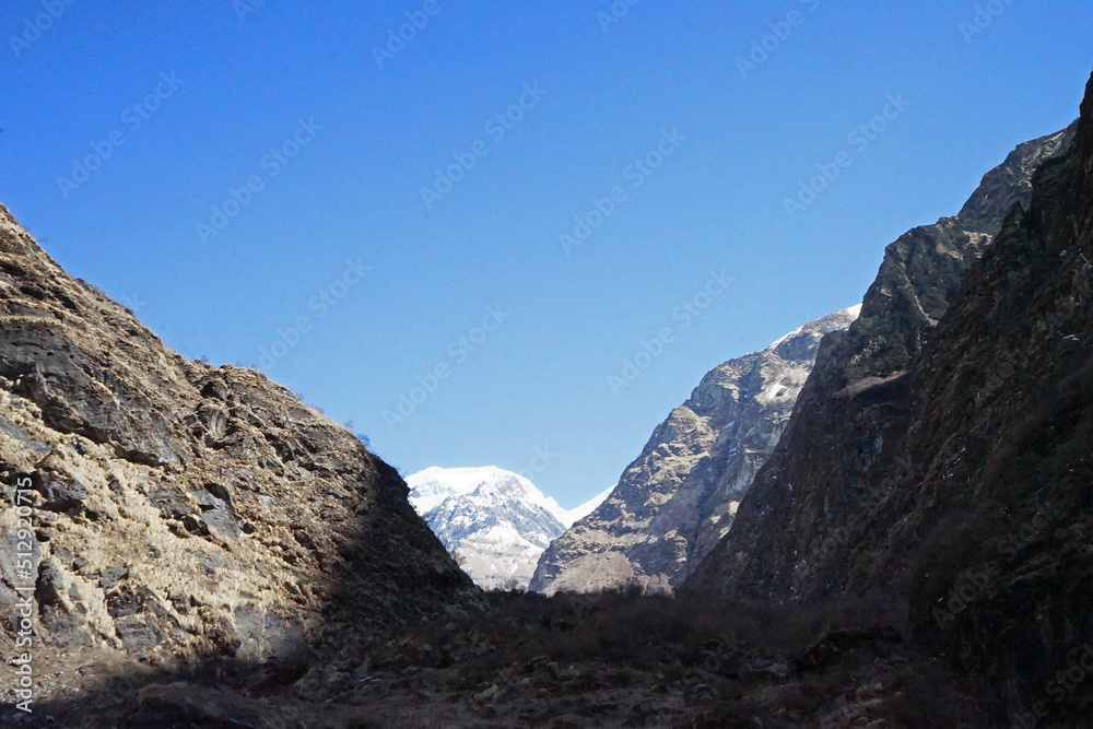 Local Nepali village among natural landscape view of snowcapped mountain cliff and cloudy blue sky- Nepal