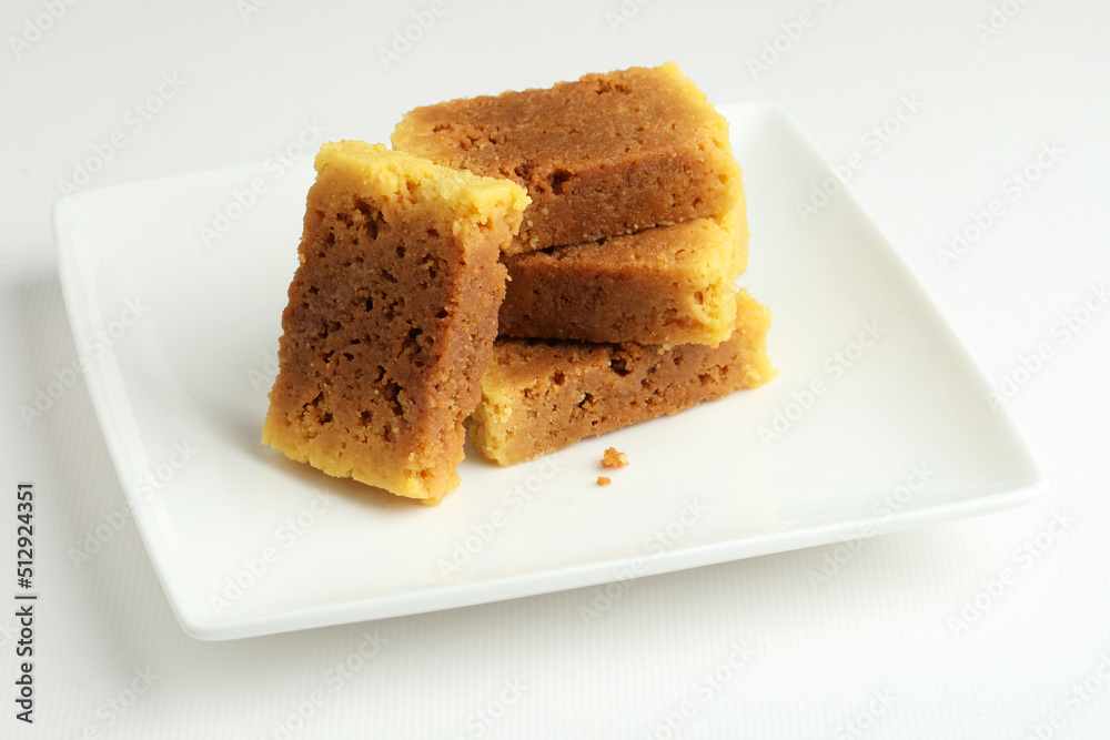 An Indian sweet originated from Mysore made from Ghee called mysore pak served on a white plate on a white background An Indian sweet originated from Mysore made from Ghee called mysore pak served on a white plate on a white background