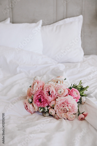Close up shot of a gorgeous bouquet of peonies and ranunculus flowers on the empty unmade bed with white sheets. A morning romantic surprize. Copy space for text, background, top view, natural light.