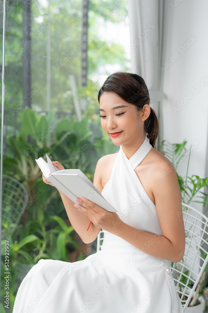 portrait of a smiling charming girl reading book while sitting on chair with plants portrait of a smiling charming girl reading book while sitting on chair with plants