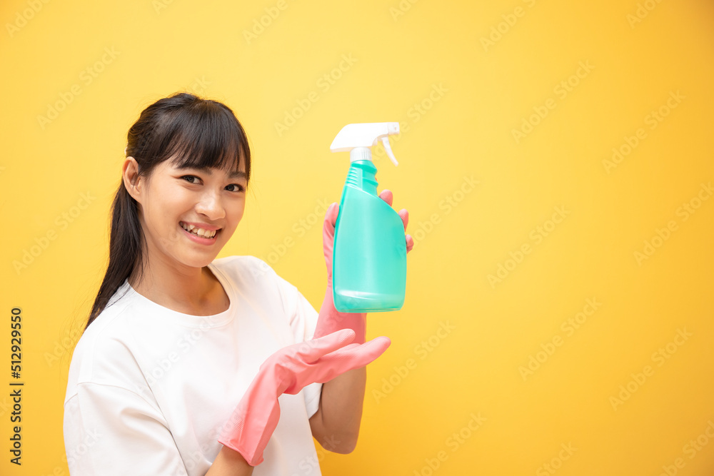 Beautiful young Asian woman with long hair in pink rubber gloves and bottle of spray cleaning on a yellow background