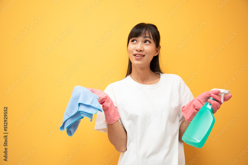 Beautiful young woman with long hair in pink rubber gloves and bottle of spray cleaning and blue table cloth on a yellow background. Surprised and excited mood Beautiful young woman with long hair in pink rubber gloves and bottle of spray cleaning and blue table cloth on a yellow background. Surprised and excited mood