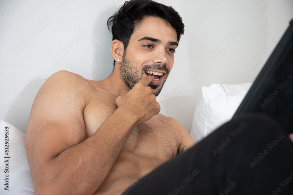 Handsome man watches an adult video on a tablet while sitting on the bed.  Concept of porn, men's needs and loneliness. Stock Photo | Adobe Stock