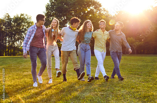 Happy best friends having fun outside in summer. Six joyful beautiful young multiethnic people enjoying good weather, walking on green grass in park, talking, laughing and having great time together