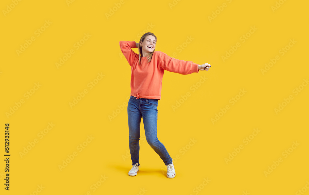 Happy beautiful young girl having fun in a modern studio. Full length shot of a cheerful woman in comfortable casual wear laughing and dancing against a vibrant yellow colour background Happy beautiful young girl having fun in a modern studio. Full length shot of a cheerful woman in comfortable casual wear laughing and dancing against a vibrant yellow colour background