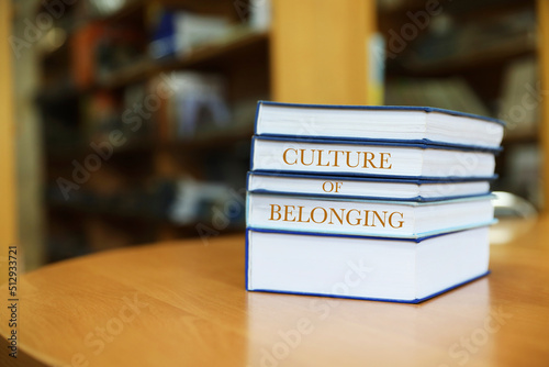 Stack of books with phrase Culture of Belonging on table in library. Space for text © New Africa