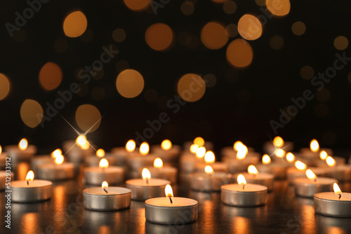 Many burning candles on table against dark background with blurred lights. Bokeh effect