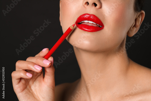 Young woman with beautiful red lip pencil on black background  closeup