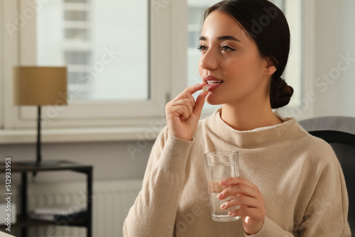 Young woman with glass of water taking dietary supplement pill indoors, space for text photo