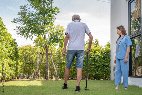 Smiling caregiver helping happy elderly man to walk in nursing home