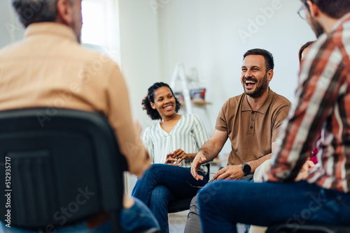 Man laughing while talking to the people, sitting in a circle, during the group therapy.
